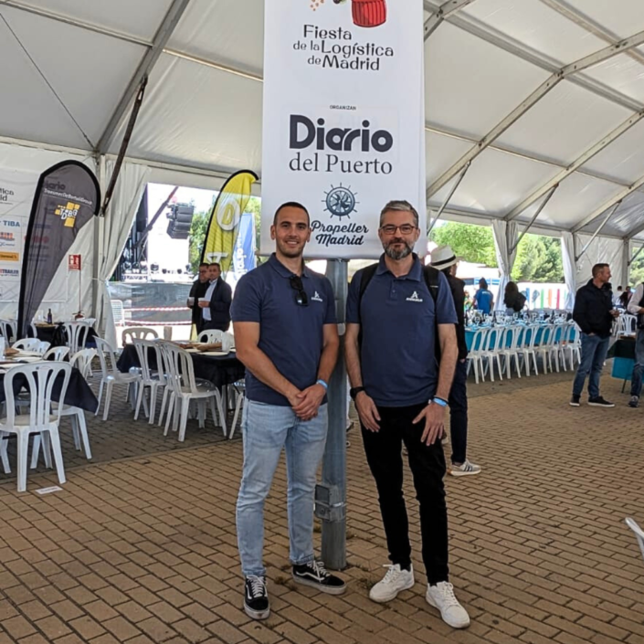 Dos miembros del equipo de Andamur frente a un banner de la Fiesta de la Logística